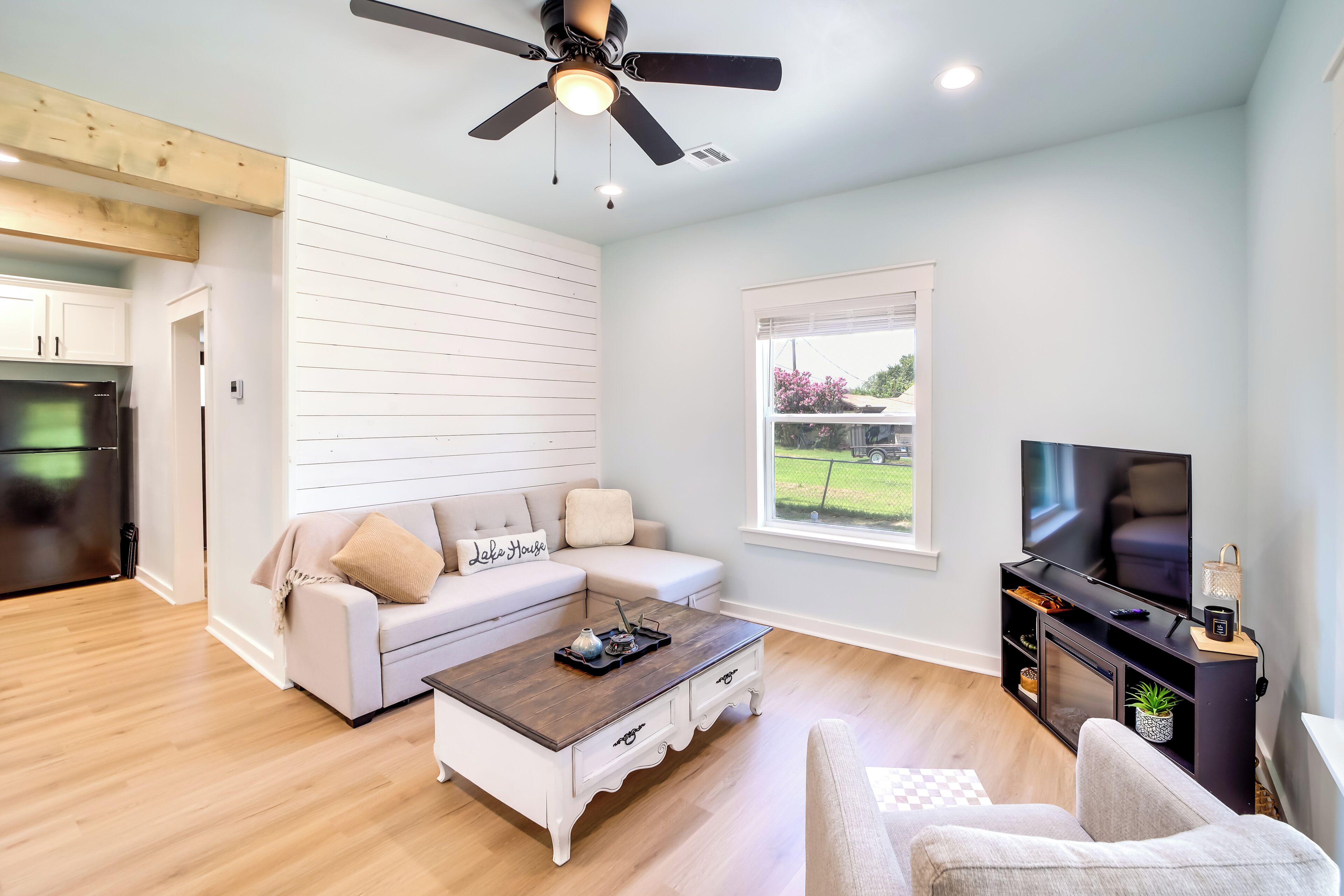 A modern living room with a white sofa, a wooden coffee table, a TV stand, and a ceiling fan.