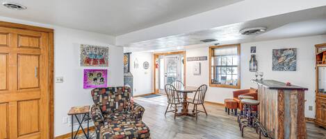 Un amplio espacio habitable con un piso de madera, un sillón estampado, una mesa de comedor con sillas y una zona de bar.