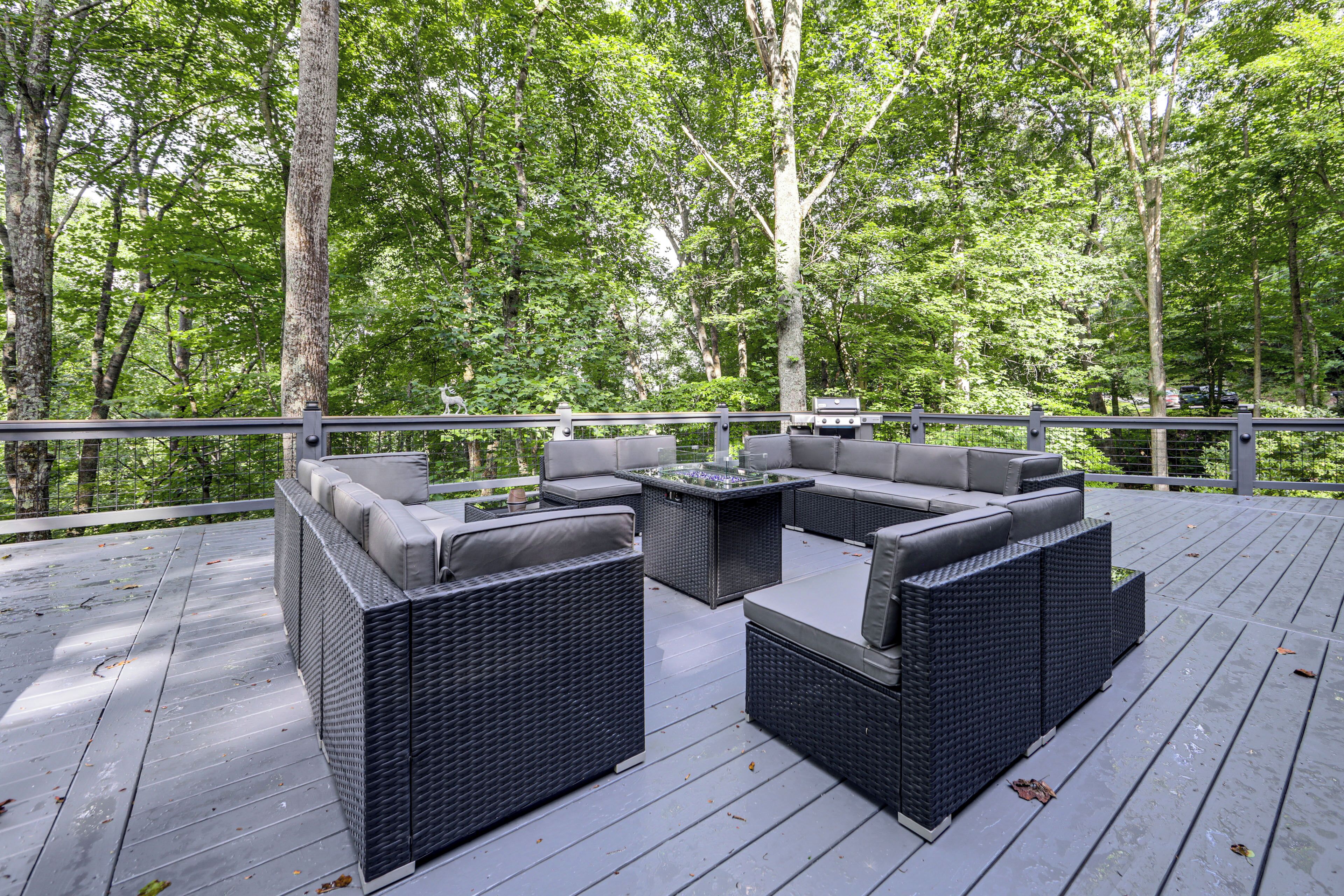 Terraza al aire libre con mobiliario de mimbre y una mesa con cubierta de vidrio, rodeada de árboles.