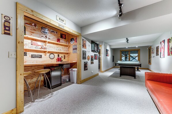 Un espace bar avec des tabourets, une table de billard et diverses décorations murales.