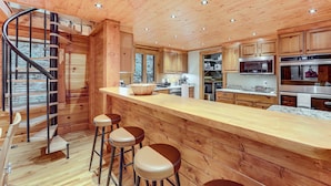 A wooden cabin interior with a kitchen, bar area, and spiral staircase. - Luxe Smoky Mountains Cabin w/ Hot Tub & Views! (Waynesville)