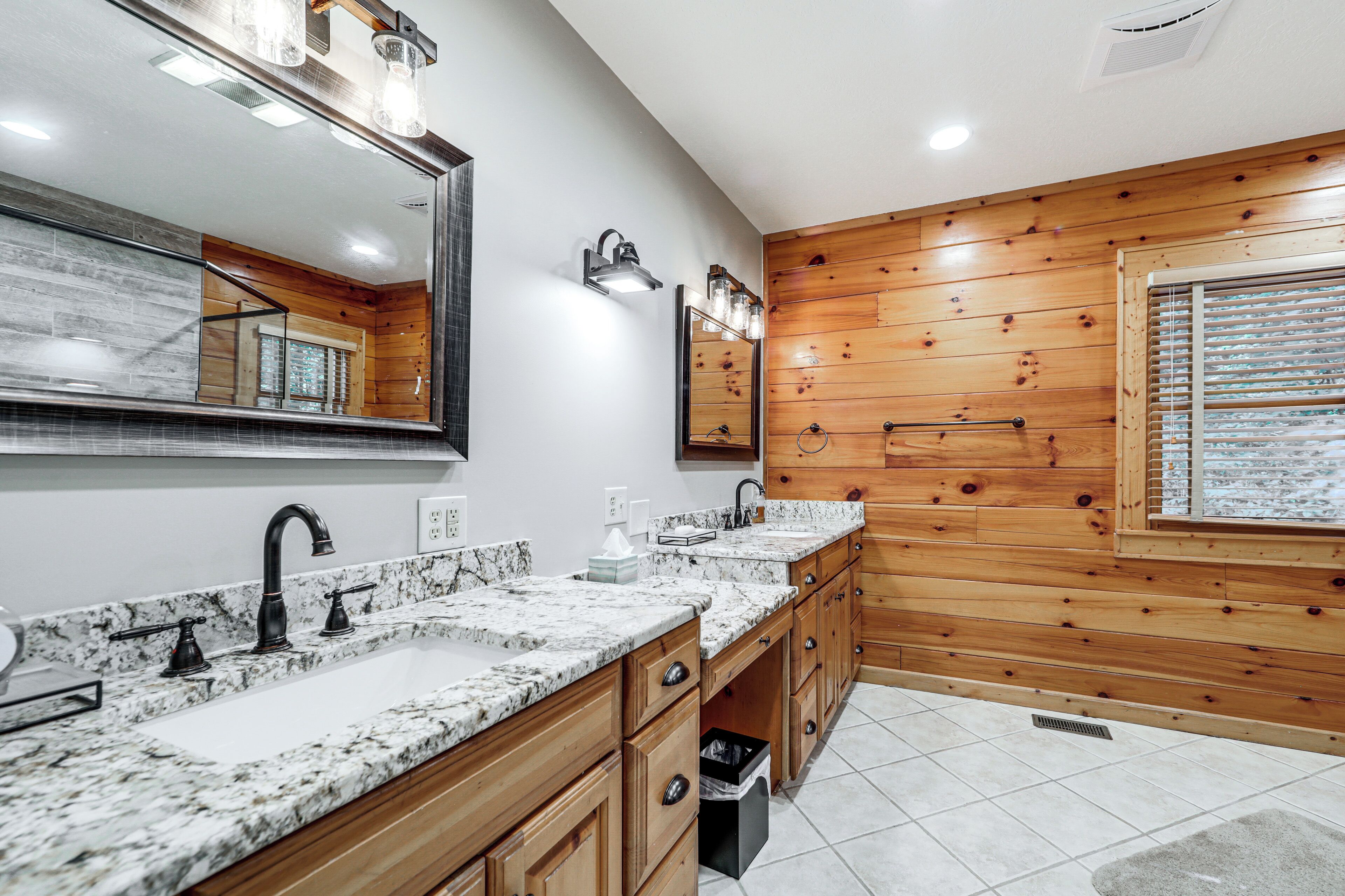 Un bagno moderno con rivestimenti in legno, uno specchio grande e un piano di lavoro in granito.