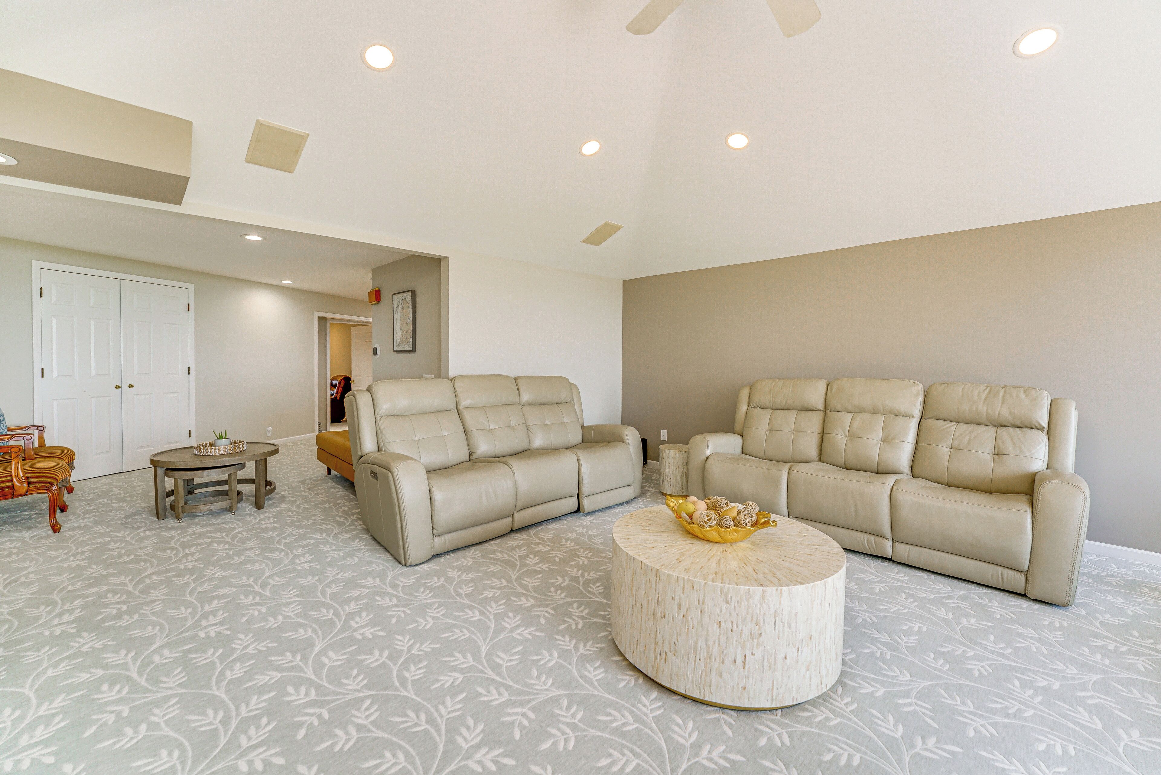 A spacious living room with two beige sofas, a round coffee table, and a patterned carpet.