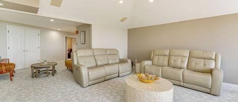 A spacious living room with two beige sofas, a round coffee table, and a patterned carpet.