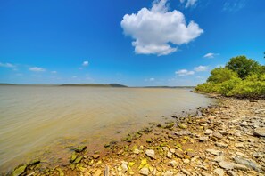 A rocky shoreline with calm water, a clear sky, and distant land.