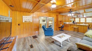 A cabin interior with wooden walls, a blue recliner, a white coffee table, and a kitchen area.