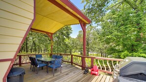A covered outdoor deck with a table and chairs, a grill, and a trash can.