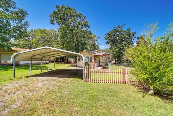 A covered outdoor area with a white fence, a house in the background, and trees.