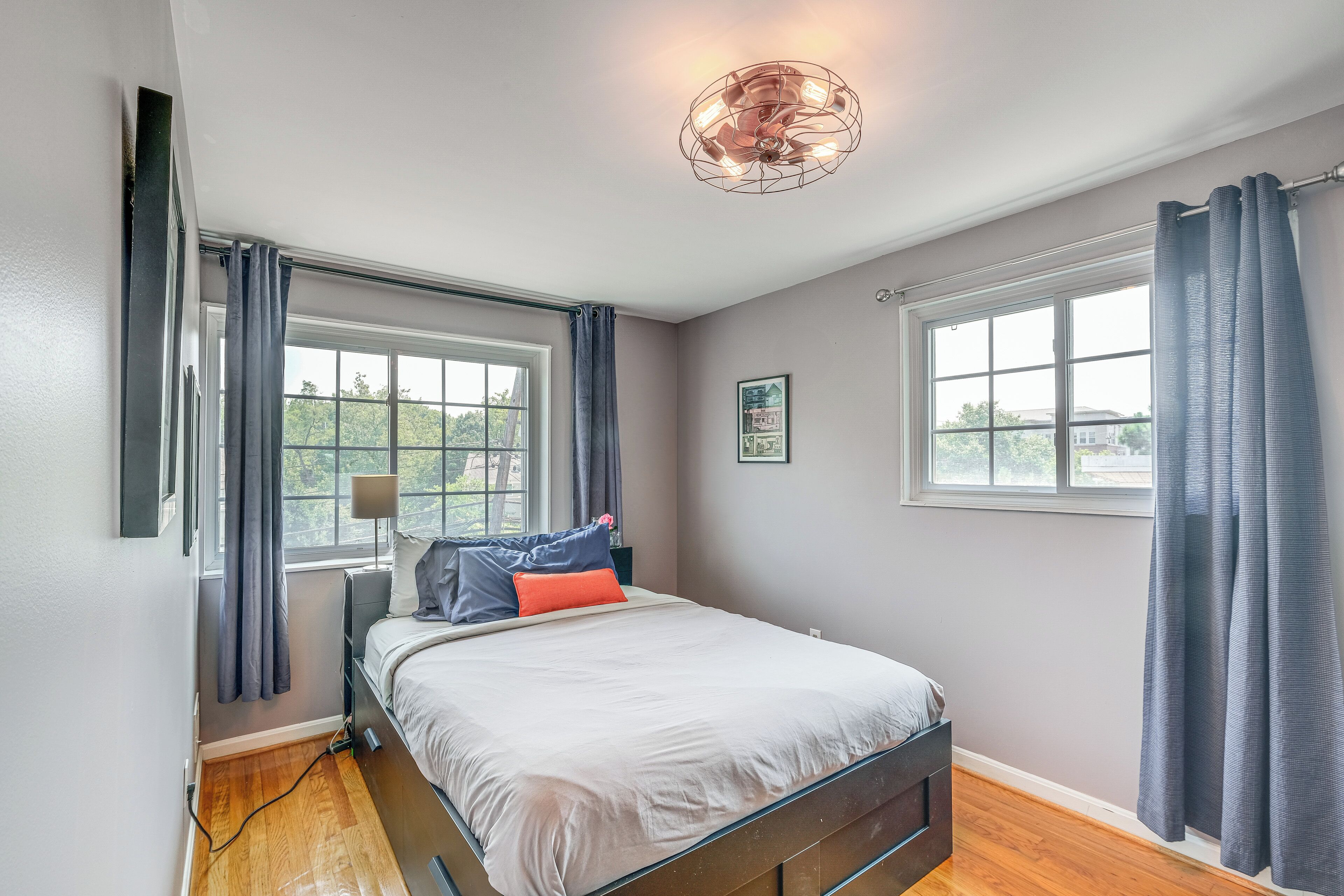 A bedroom with a bed, two windows, a ceiling light fixture, and a framed picture on the wall.