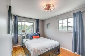 Ein Schlafzimmer mit einem Bett, zwei Fenstern, einer Deckenleuchte und einem gerahmten Bild an der Wand.