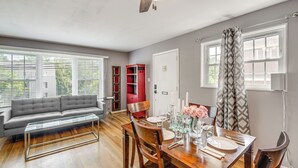 Un salon moderne avec un canapé gris, une table à manger en bois pour quatre personnes et un ventilateur de plafond.