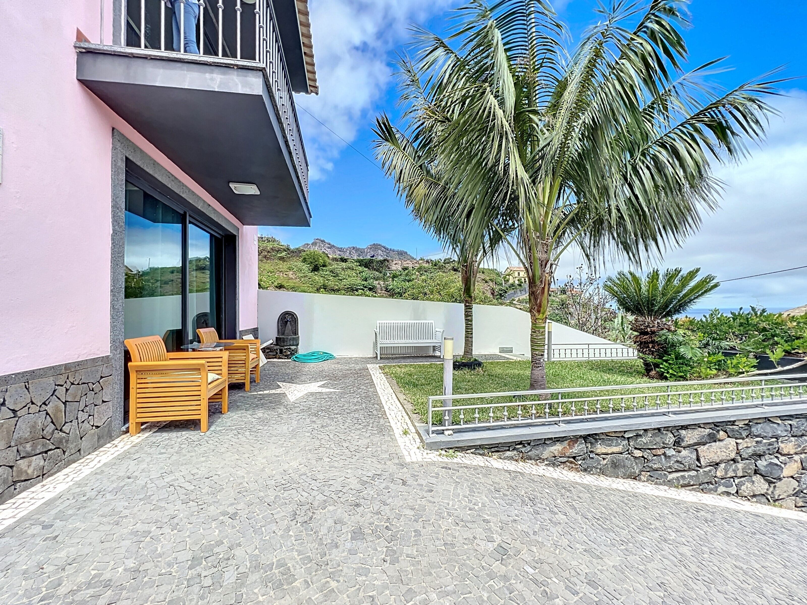 A modern building with a balcony, stone walls, and a view of a mountainous landscape.