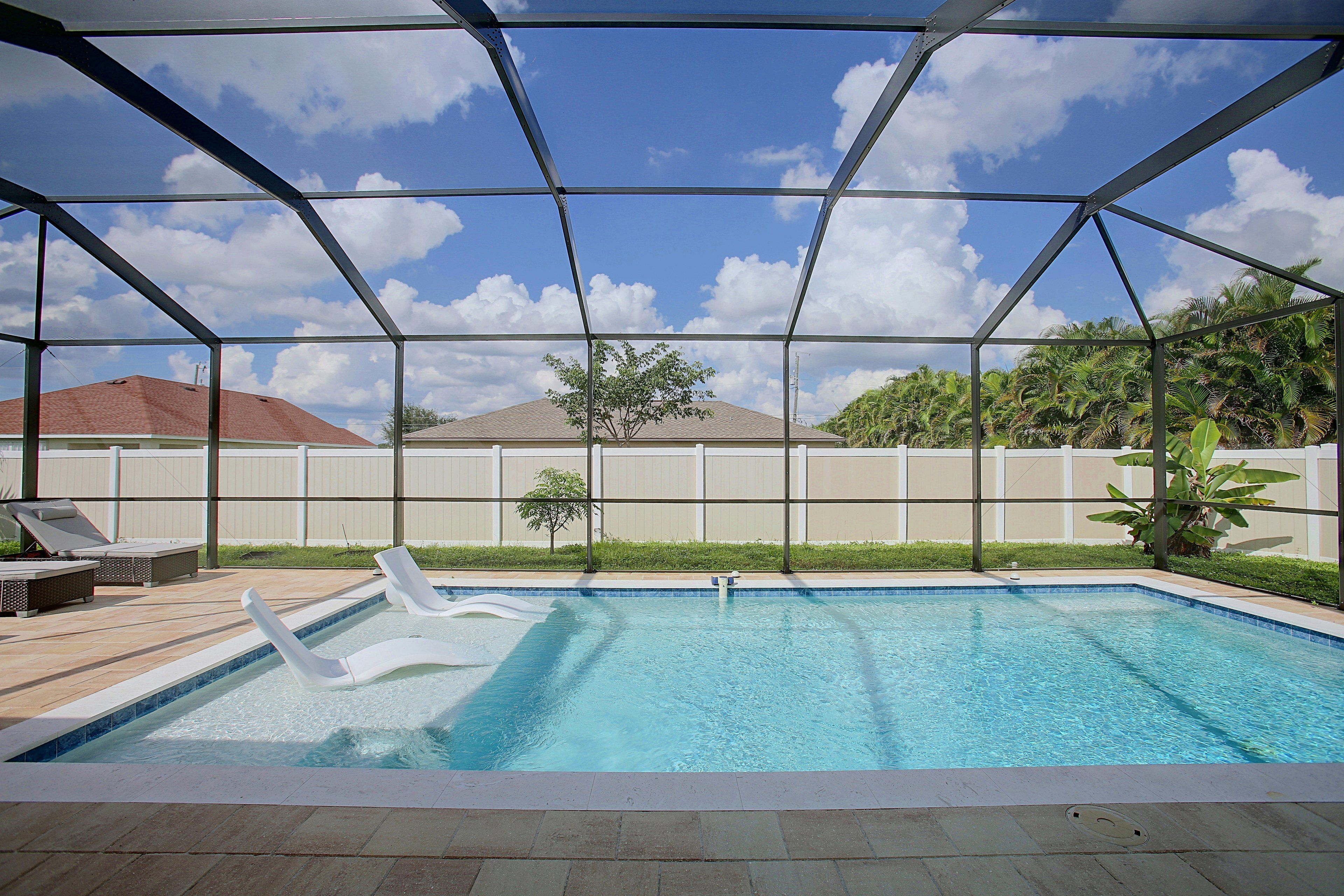 A swimming pool with a covered area, surrounded by a fence, and a tree in the background.