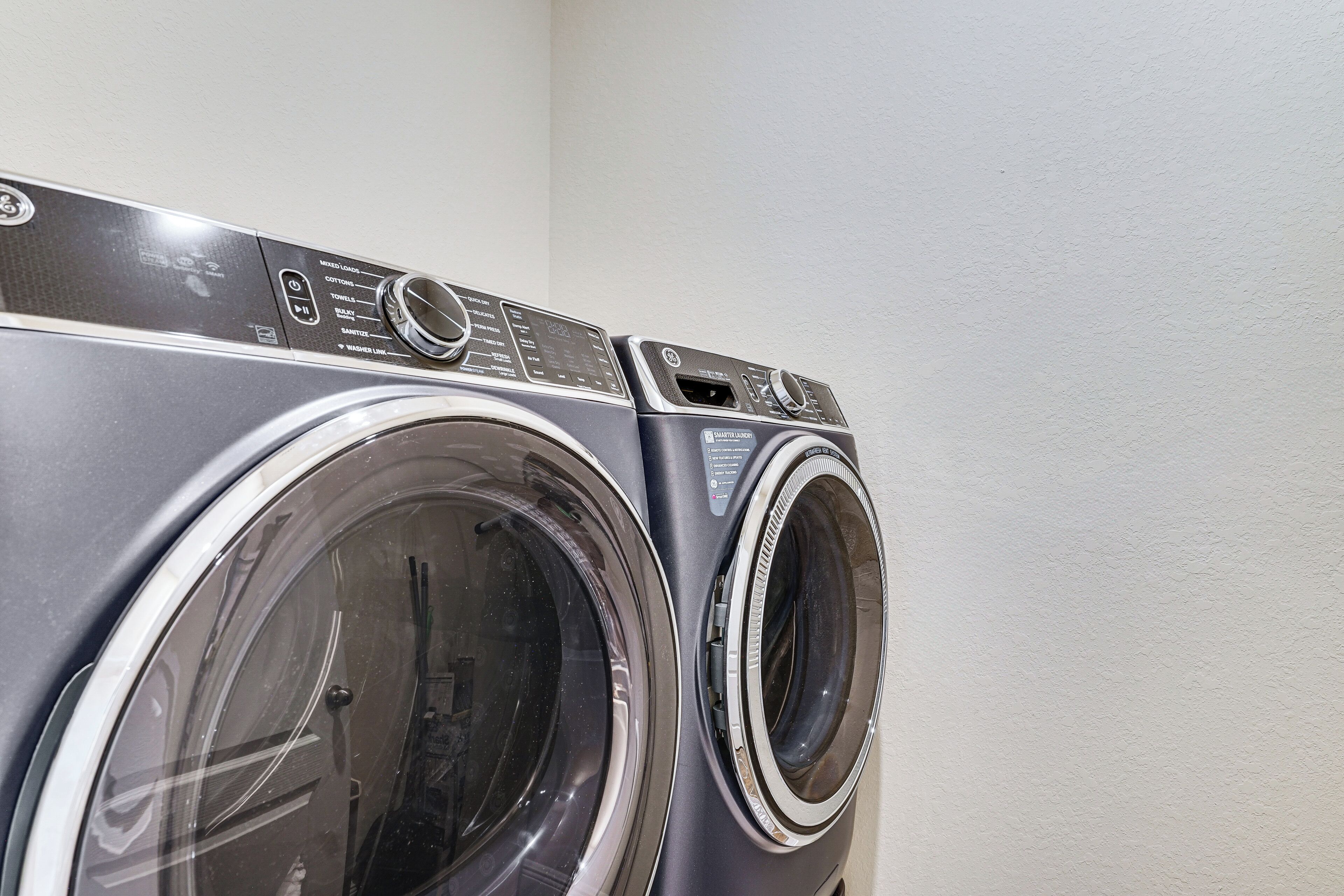 Une vue de face d’un lave-linge à chargement frontal, avec son panneau de commande, un sèche-linge et un panneau de commande fixé au mur.