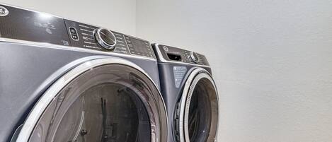 Une vue de face d’un lave-linge à chargement frontal, avec son panneau de commande, un sèche-linge et un panneau de commande fixé au mur.