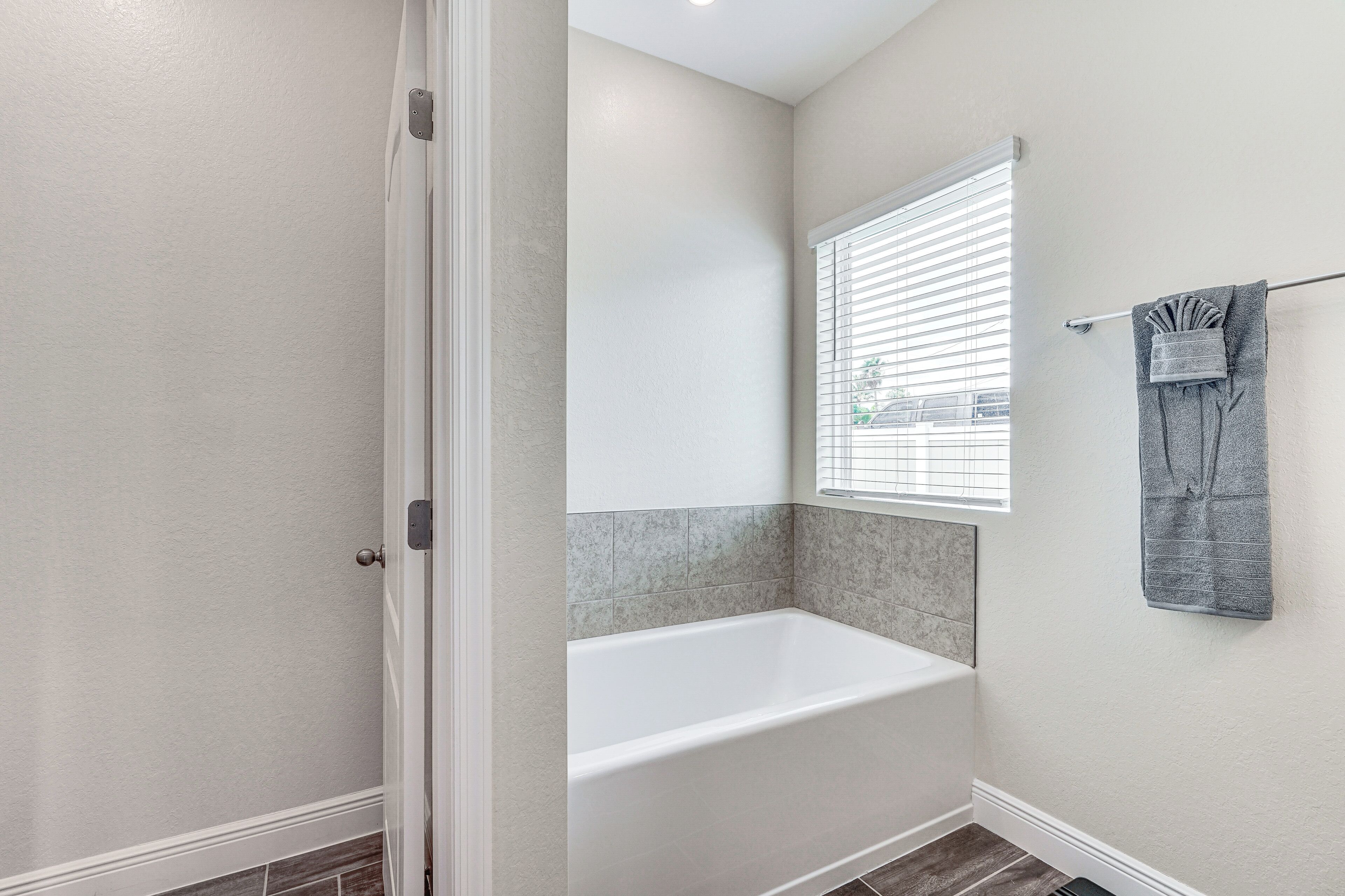 A bathroom with a bathtub, a window with blinds, and a towel rack with a towel.