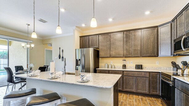 A modern kitchen with dark wood cabinets, stainless steel appliances, and a marble island with bar stools. - 4 Mi to Golf: Gem w/ Pool & Lanai in Cape Coral (Cape Coral)