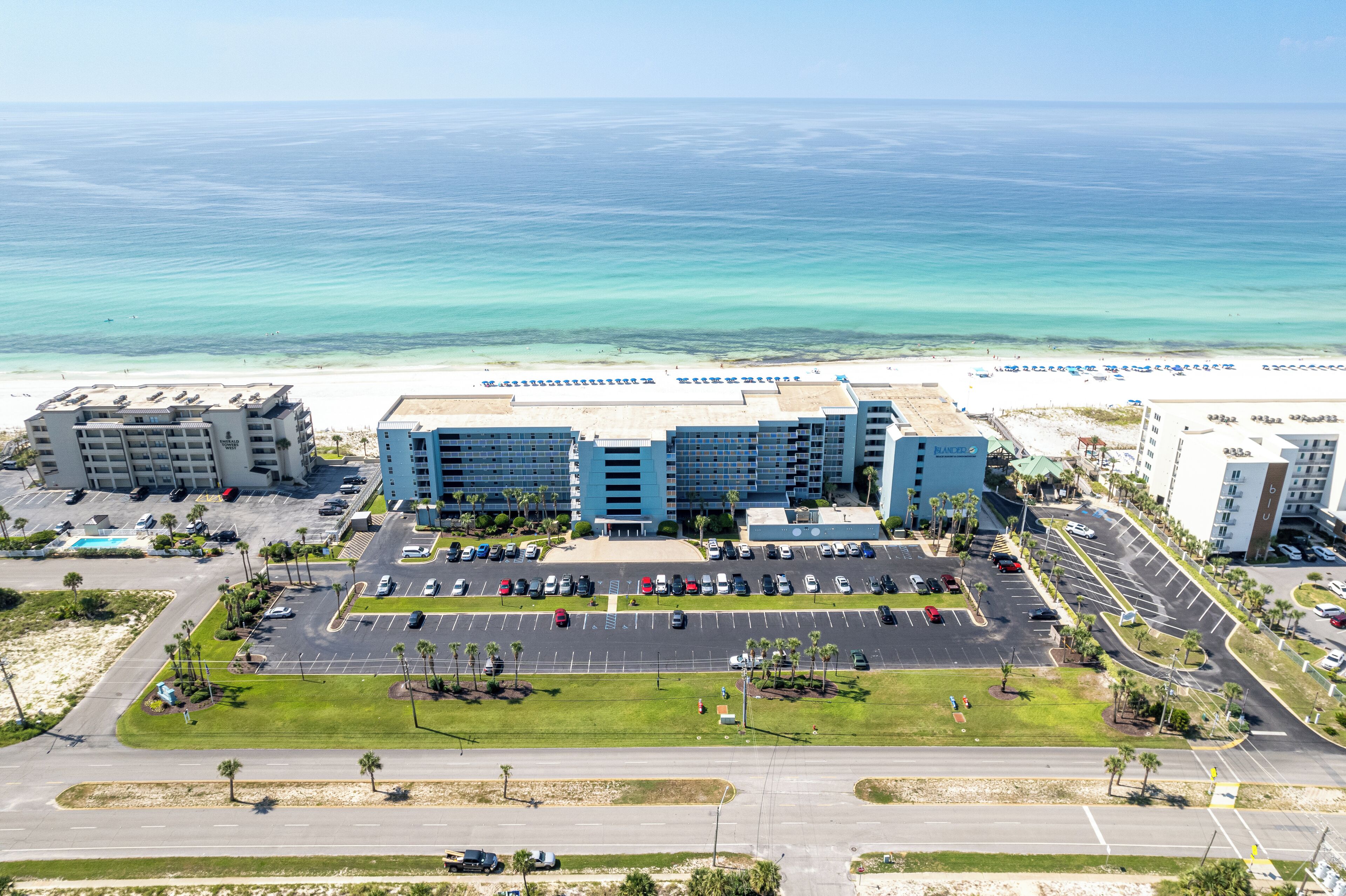 A hotel with a parking lot, a beach view, and a pool.