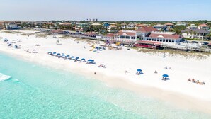 Een strand met helder turquoise water, een zandstrand en verschillende strandparasols.