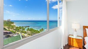Une chambre d’hôtel dotée d’une grande fenêtre donnant sur l’océan et un paysage tropical.