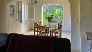 Een eetgedeelte met een glazen tafel en stoelen, een potplant en uitzicht op groen door een raam.
