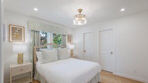 A neatly arranged bedroom with a large bed, bedside tables, a hanging light fixture, and a view of the outdoors through a window with patterned curtains. - Resort-Style 3BR/3BA • Pool & Spa • Gated (Houston)