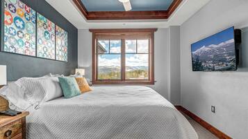 Un dormitorio con una cama grande, un ventilador de techo, un ventanal con vistas a la montaña y coloridos adornos en la pared.