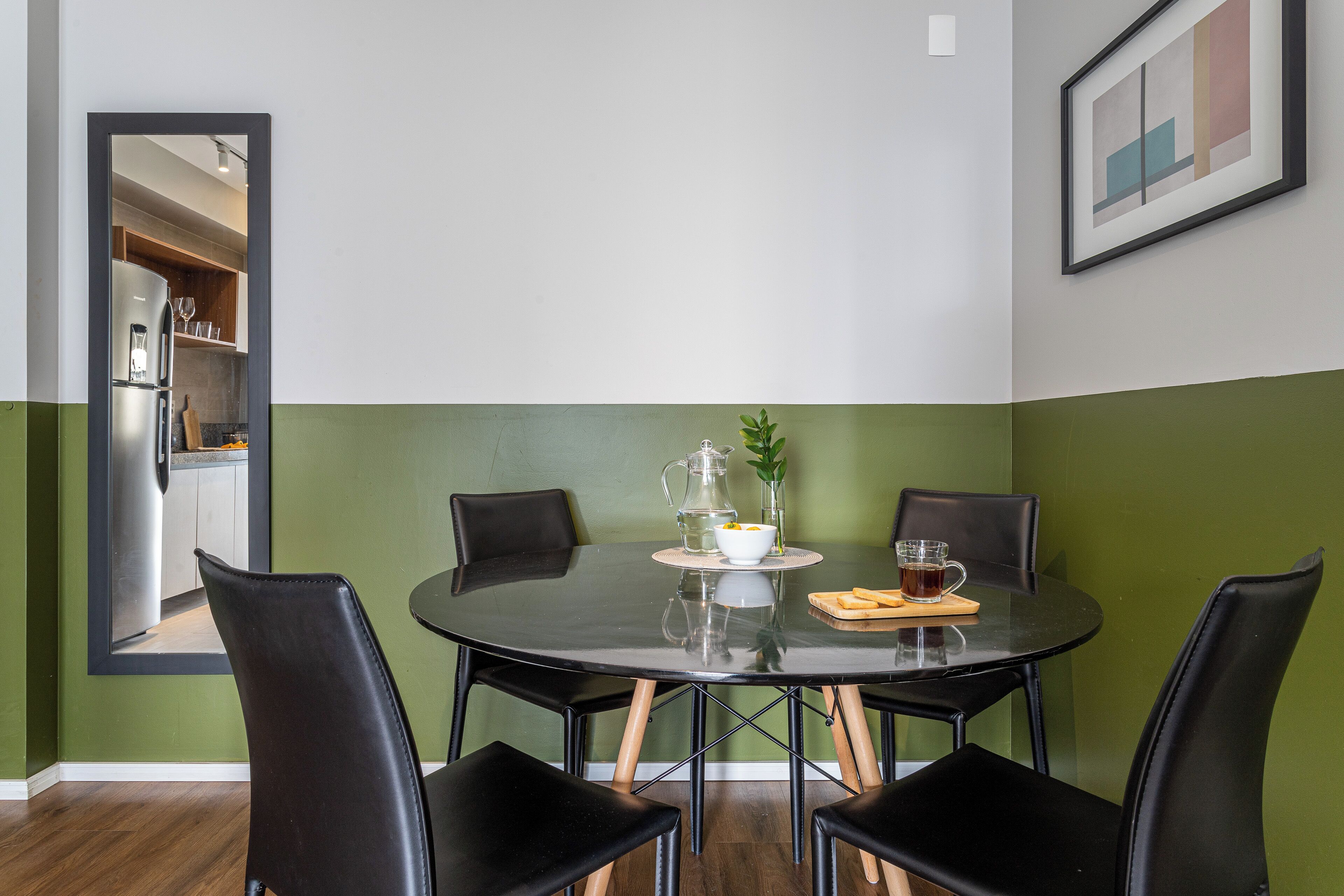 A dining area with a round table, four black chairs, a pitcher, a bowl, and a plate with bread.