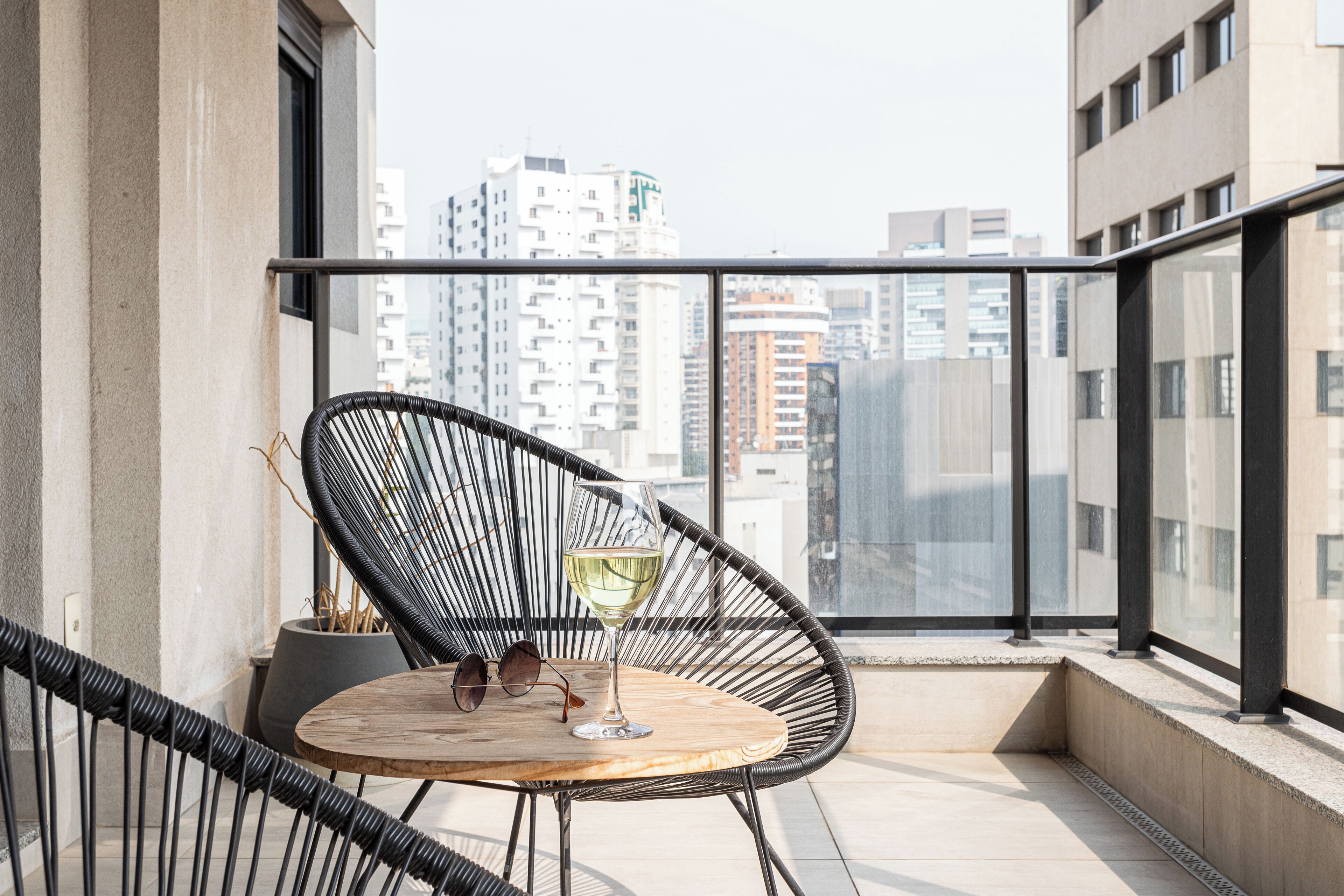 A balcony with a round table, a black wicker chair, and a glass of white wine.
