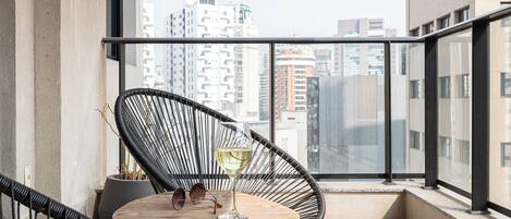 A balcony with a round table, a black wicker chair, and a glass of white wine.