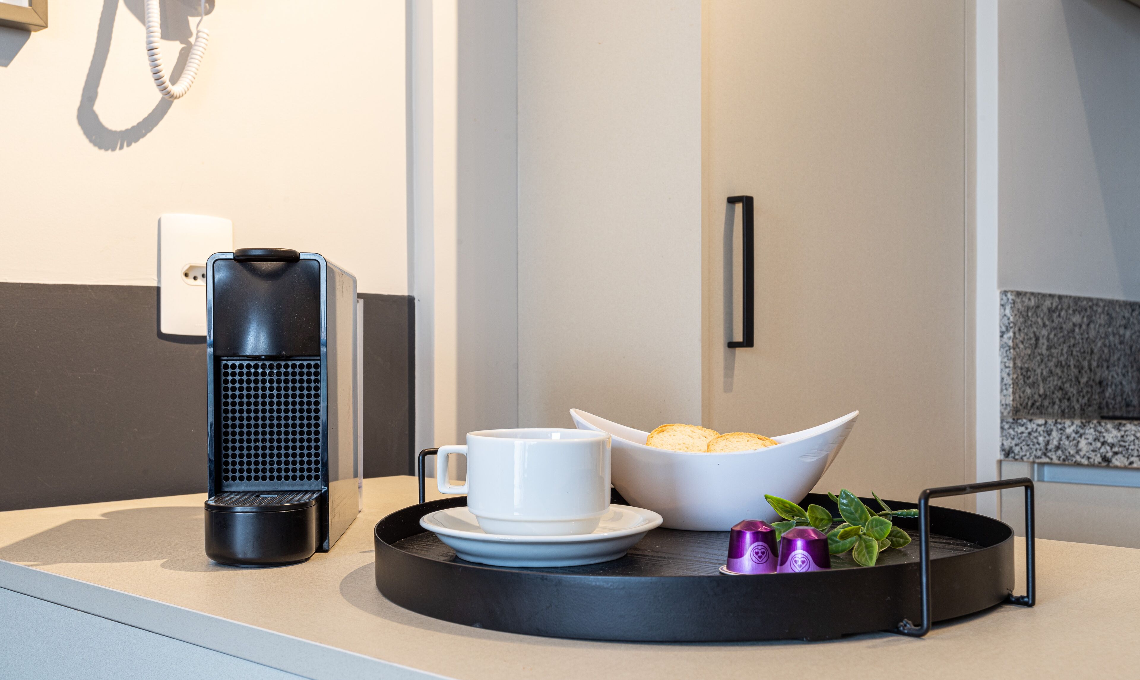 Una cocina moderna con una cafetera, una taza blanca, un cuenco de galletas y una planta pequeña sobre una bandeja.