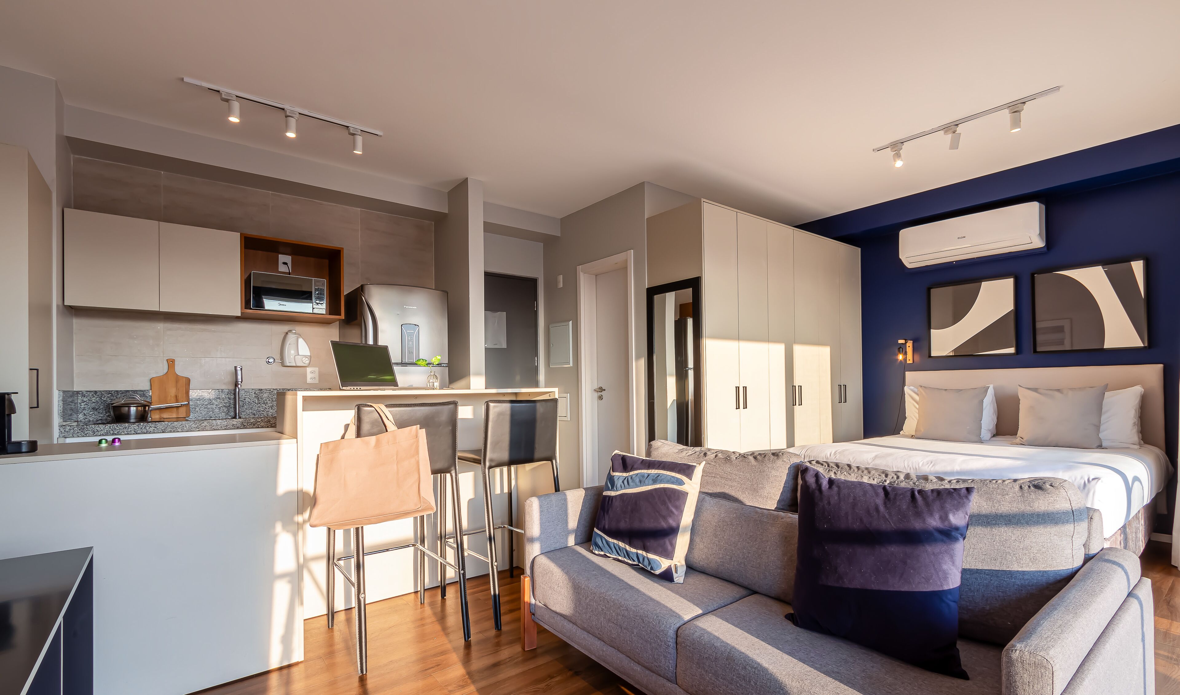 Una habitación de hotel moderna con kitchenette, sofá cama y zona de comedor.