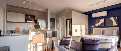 Una habitación de hotel moderna con kitchenette, sofá cama y zona de comedor.