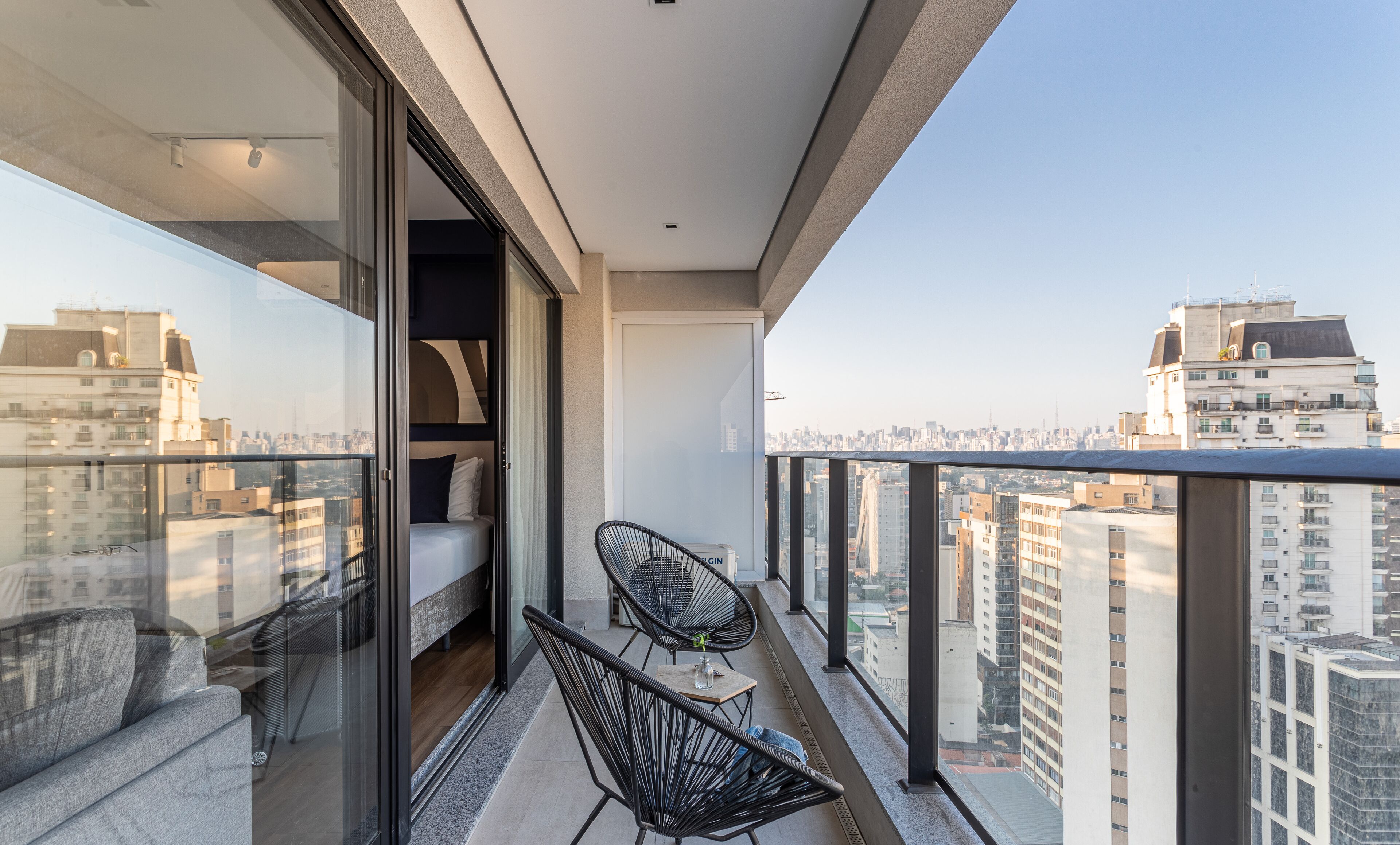 Un balcon avec un lit, deux chaises et une vue sur le paysage urbain.