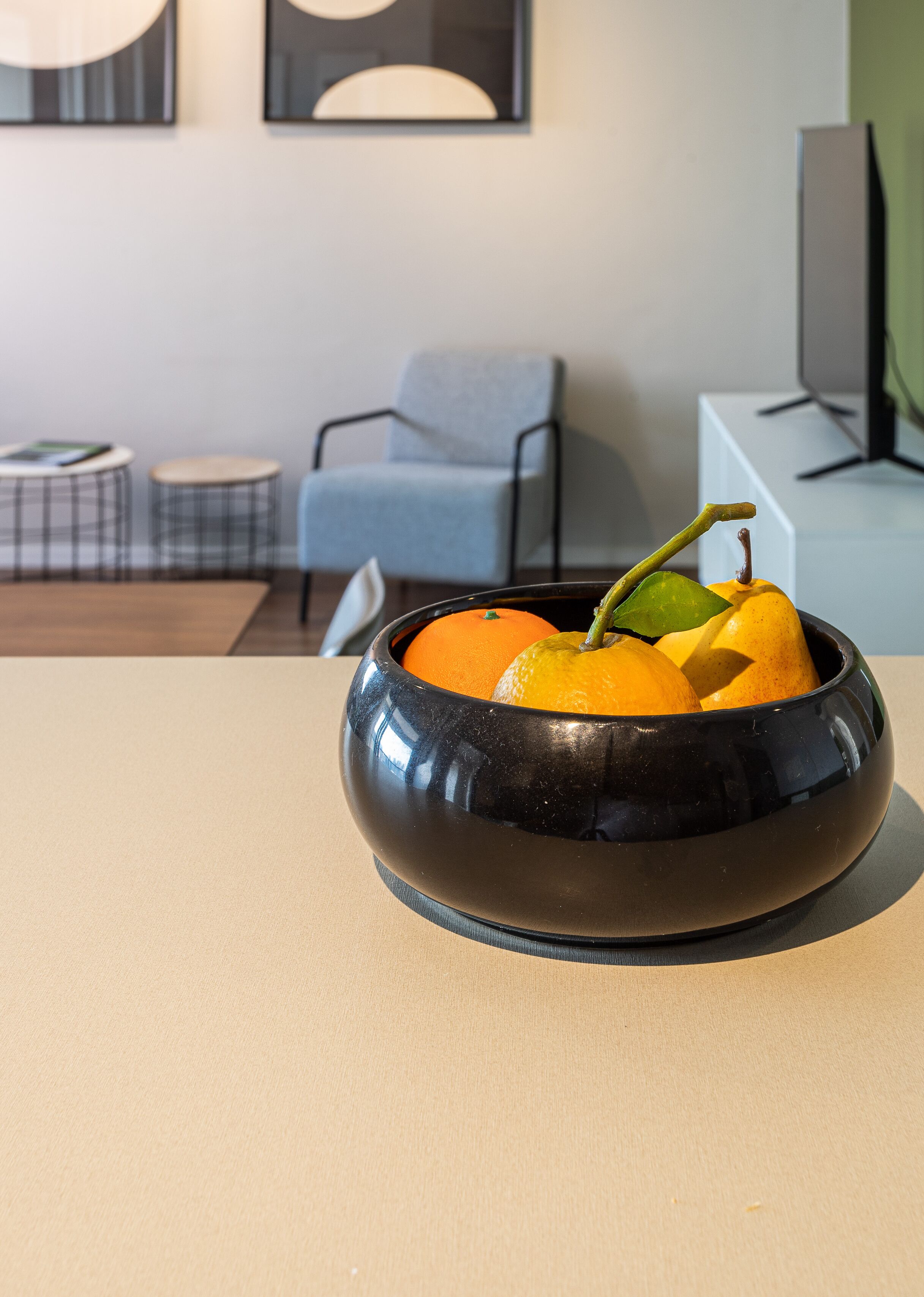 A modern living room with a black bowl containing oranges and a banana on a beige table.