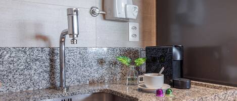 A kitchen with a granite countertop, stainless steel sink, and a coffee machine.