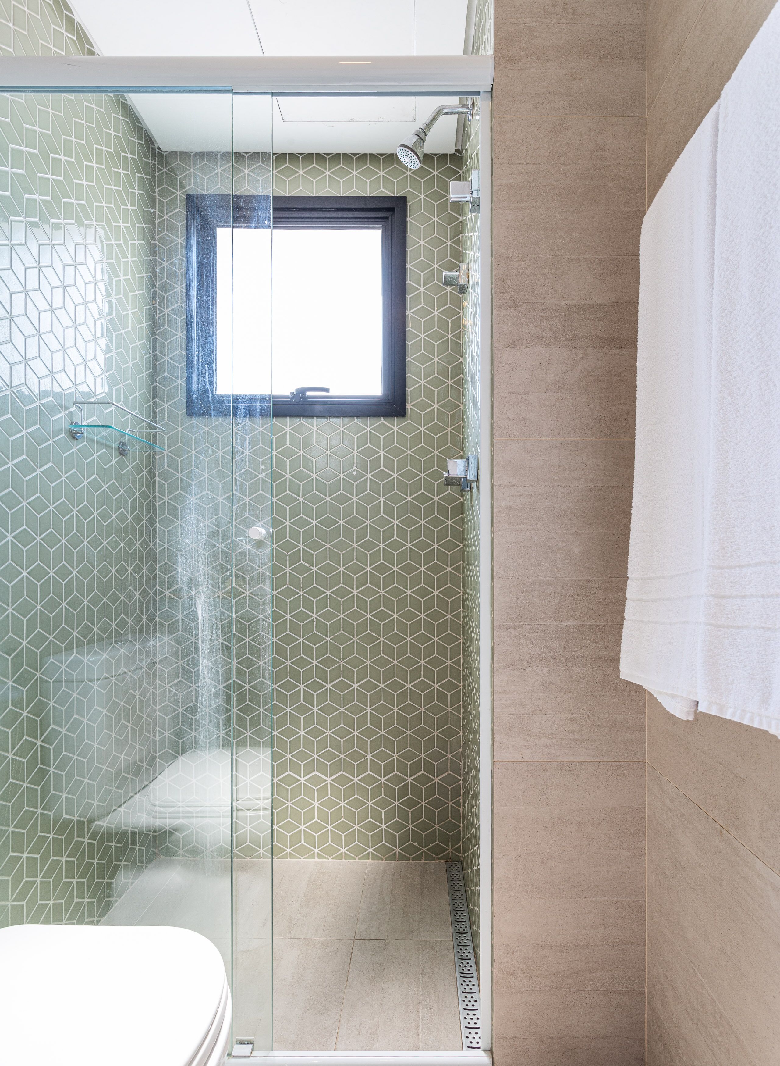 A modern bathroom with a glass-enclosed shower, a window, and a white towel hanging on the wall.