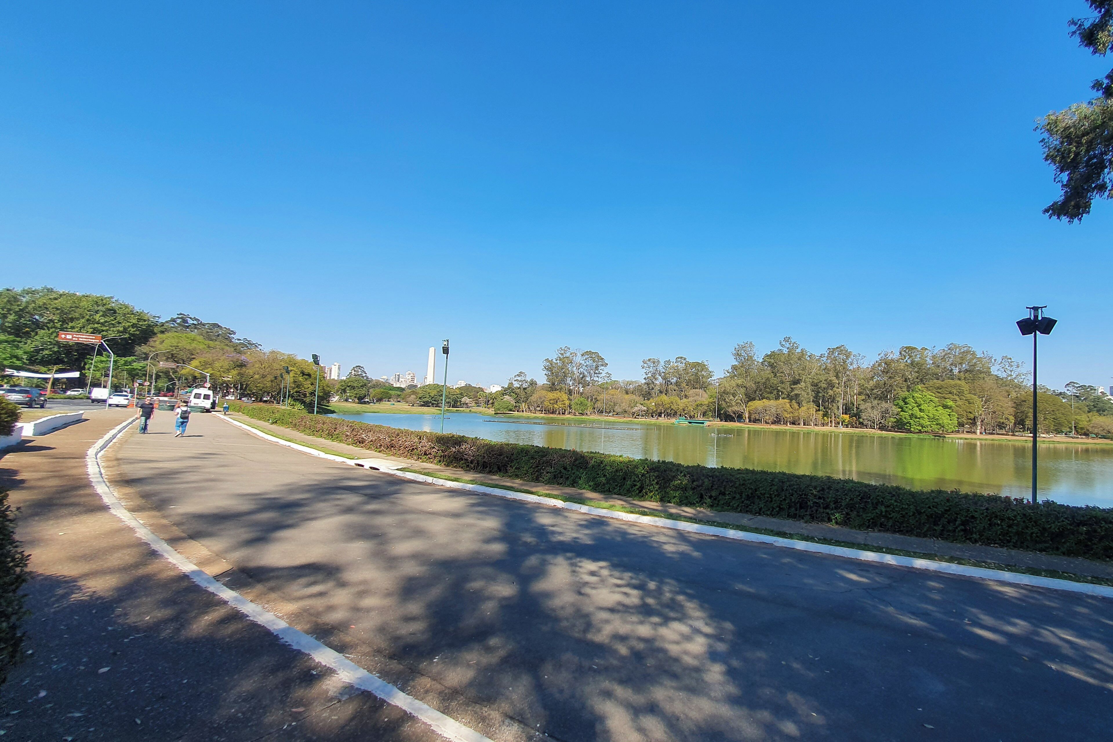 A curved road with a lake, trees, and a distant building.