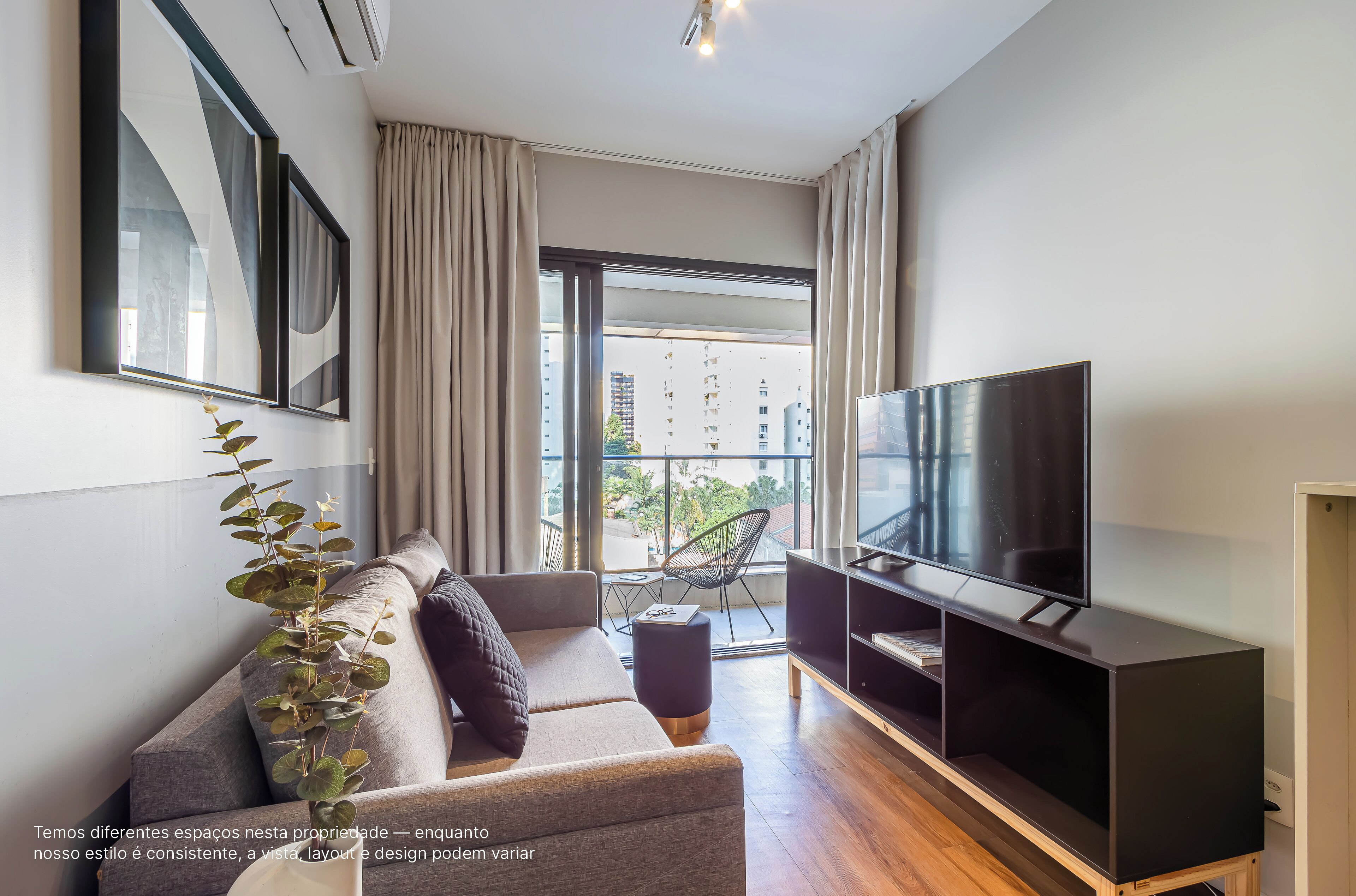Un salon moderne avec un canapé, un téléviseur et un balcon offrant une vue sur les immeubles.