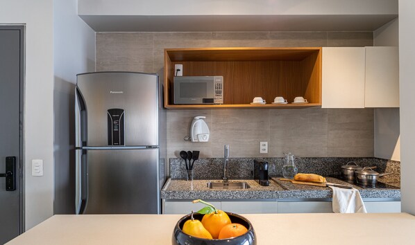 A modern kitchen with a stainless steel refrigerator, a microwave, and a coffee maker. - Helbor Nun Vila Nova by Viva - Apartamentos completos próximo ao Parque do Ibirapuera (São Paulo)