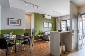 A modern living space with a dining area, a sofa, and a small table with a plant. - Helbor Nun Vila Nova by Viva - Apartamentos completos próximo ao Parque do Ibirapuera (São Paulo)