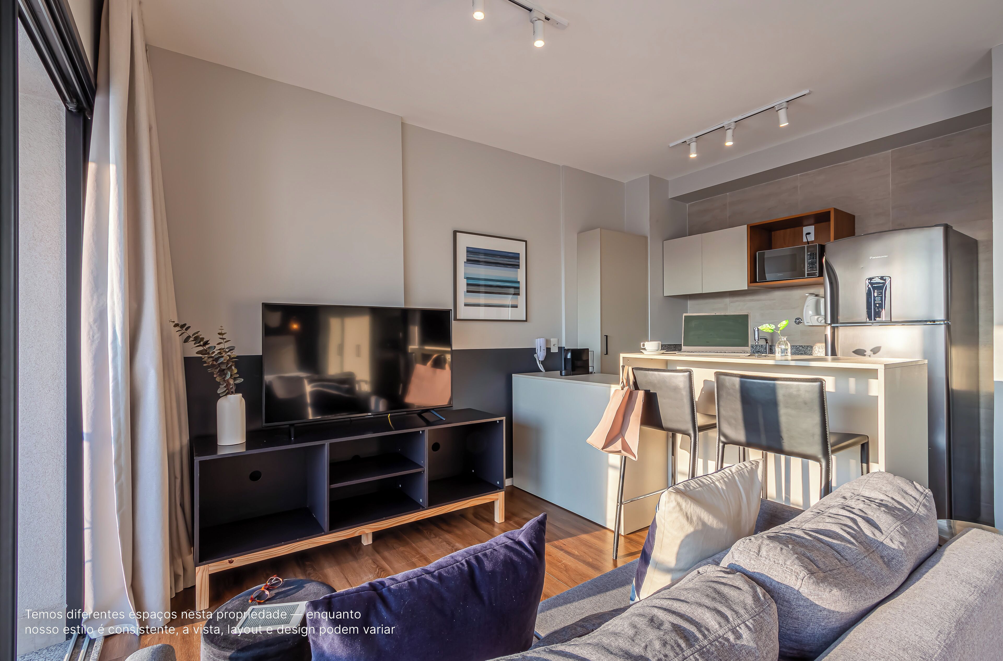 A modern living room with a flat-screen TV, a sofa, and a kitchen area with a microwave and refrigerator.