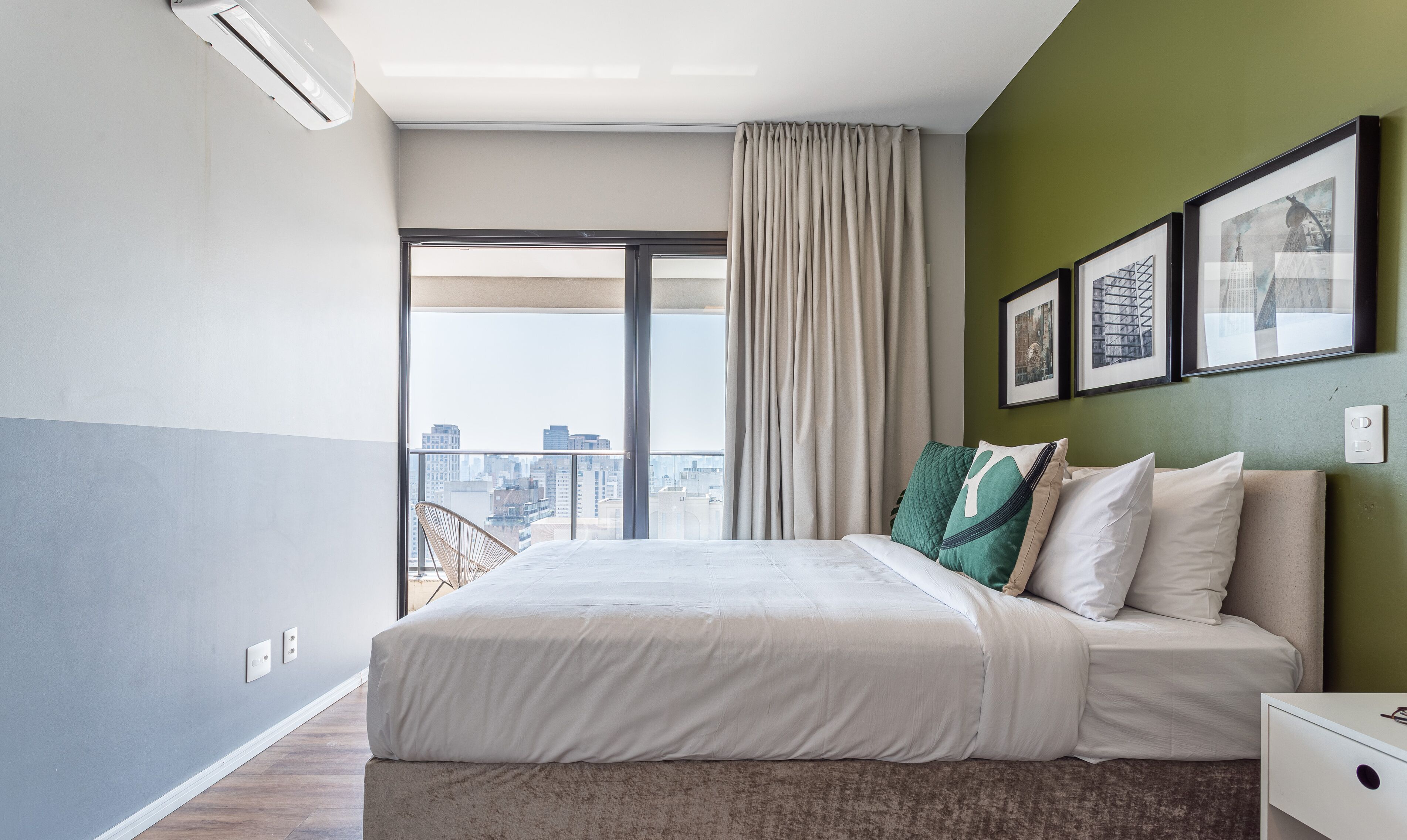 Una habitación de hotel moderna con una cama grande, vistas de la ciudad y una pared de acento verde.