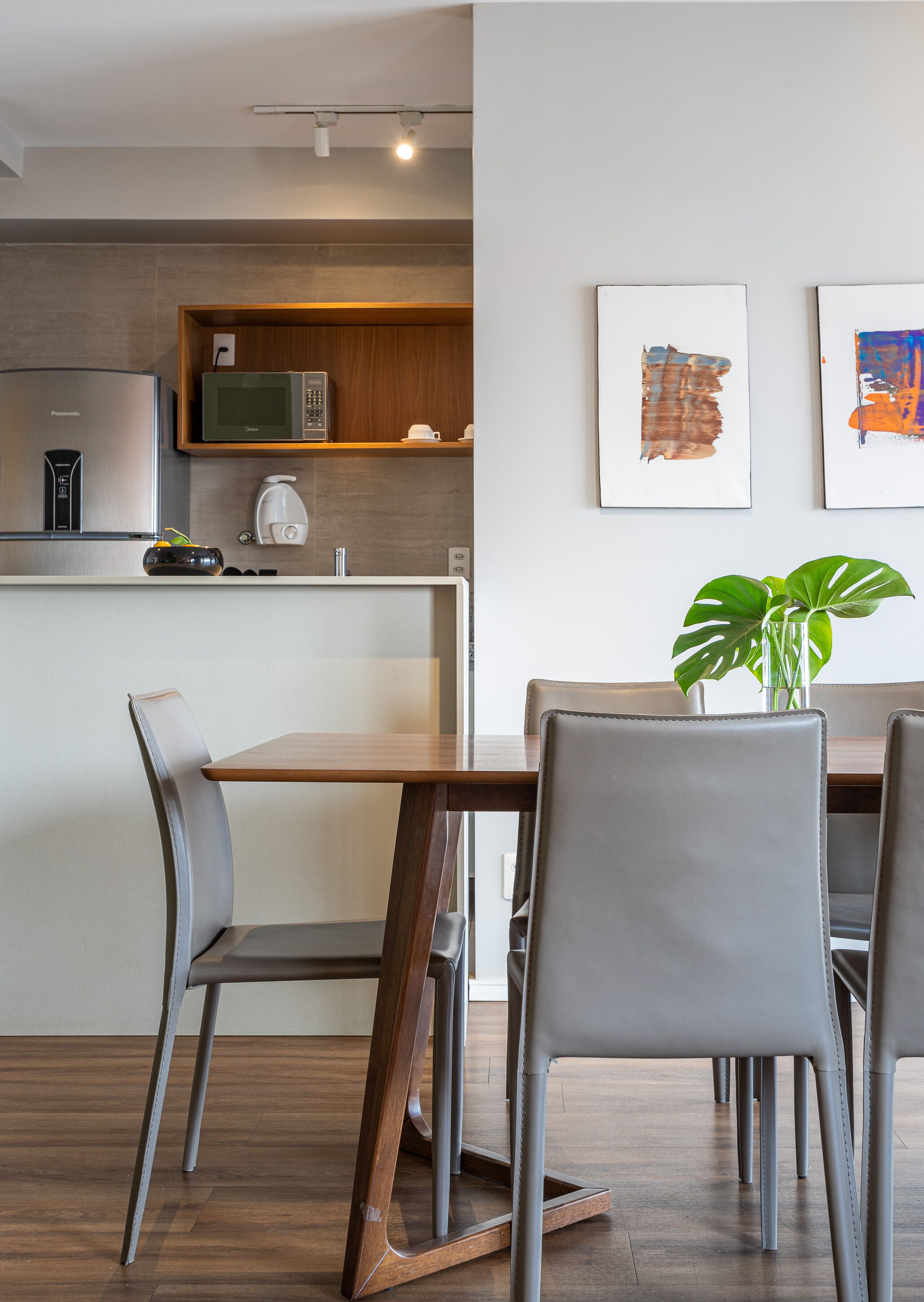 A modern kitchen with a microwave, coffee maker, and a wooden table with chairs. There are two framed artworks on the wall.