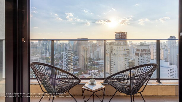 A balcony with two black wire chairs, a small table with a cup and a book, and a cityscape view.