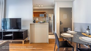 A modern kitchen with a TV, microwave, and refrigerator. There is a dining area with a table set for two.