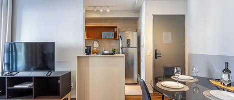 Cocina moderna con televisor, microondas y refrigerador. Hay una zona de comedor con una mesa dispuesta para dos personas.
