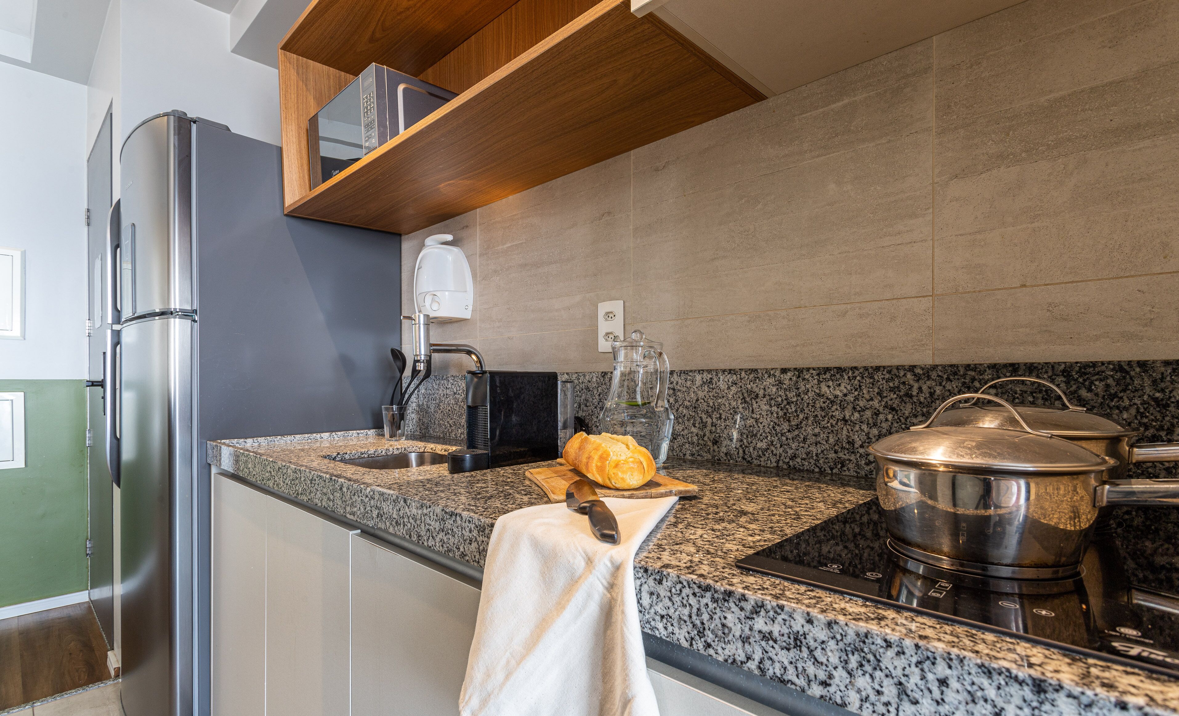 A modern kitchen with granite countertops, stainless steel appliances, and a wooden shelf above the sink.