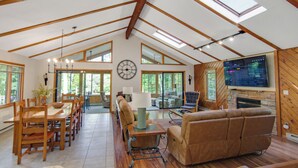 Un loft espacioso con techos altos, vigas de madera, una zona de comedor con una mesa y sillas largas, un rincón de estar acogedor con sofás y una chimenea.