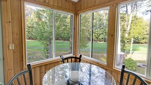 Una habitación con paneles de madera, una mesa redonda de vidrio y sillas, con ventanas amplias que dan a un paisaje verde.